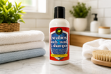 Scabies body wash & shampoo bottle on a bathroom counter with towels and a brush.