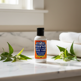 Tamed Organics Mite Marvel Anti-Itch and Anti-Mite Body Wash bottle on a white marble countertop with tea tree and neem leaves, soft natural light, and a spa-inspired setting
